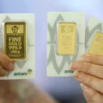 A person holding three certified Antam gold bars in 100g and 50g sizes, showcasing the official LM packaging.