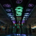 Neon Grab signs and service icons glow on the ceiling of a modern, dark interior space with escalators.