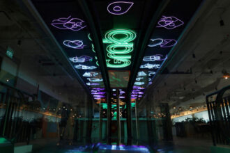 Neon Grab signs and service icons glow on the ceiling of a modern, dark interior space with escalators.