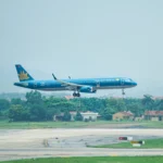 A Vietnam Airlines aircraft coming in for a landing at an airport with a lush green landscape in the background.