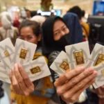 Two people proudly display several gold bars in branded certicards from Antam while at a retail store.