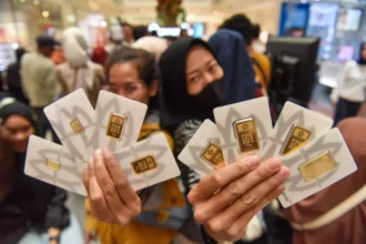 Two people proudly display several gold bars in branded certicards from Antam while at a retail store.