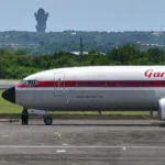 A Garuda Indonesia aircraft on the tarmac in Bali, with the iconic GWK statue visible in the distance.