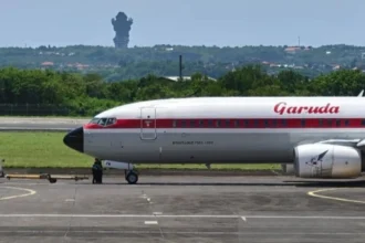 A Garuda Indonesia aircraft on the tarmac in Bali, with the iconic GWK statue visible in the distance.