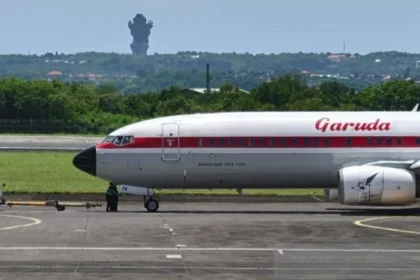 A Garuda Indonesia aircraft on the tarmac in Bali, with the iconic GWK statue visible in the distance.