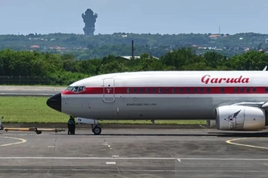 A Garuda Indonesia aircraft on the tarmac in Bali, with the iconic GWK statue visible in the distance.