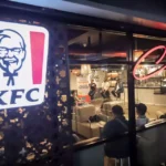 An illuminated KFC sign outside a modern restaurant outlet featuring a specialized coffee seating area.