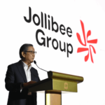Tony Tan Caktiong speaking at a podium with the Jollibee Group logo displayed prominently in the background.
