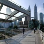 Pedestrians on a modern walkway in Kuala Lumpur, a city positioning itself as a stable hub despite the supply crisis.