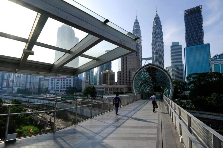 Pedestrians on a modern walkway in Kuala Lumpur, a city positioning itself as a stable hub despite the supply crisis.