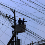 Maintenance workers on power lines, illustrating infrastructure costs monitored by the central bank.