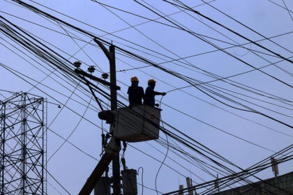 Maintenance workers on power lines, illustrating infrastructure costs monitored by the central bank.