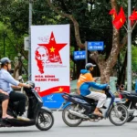 Motorcyclists riding past a Ho Chi Minh propaganda poster in a Vietnam street where DBS is expanding its presence.