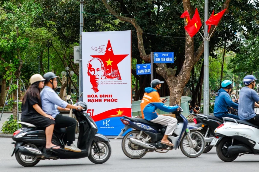 Motorcyclists riding past a Ho Chi Minh propaganda poster in a Vietnam street where DBS is expanding its presence.