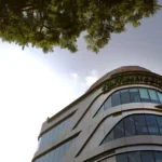 Low angle shot of the modern Raffles Medical building facade against a clear sky with green foliage.