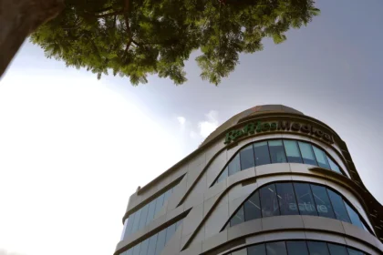 Low angle shot of the modern Raffles Medical building facade against a clear sky with green foliage.