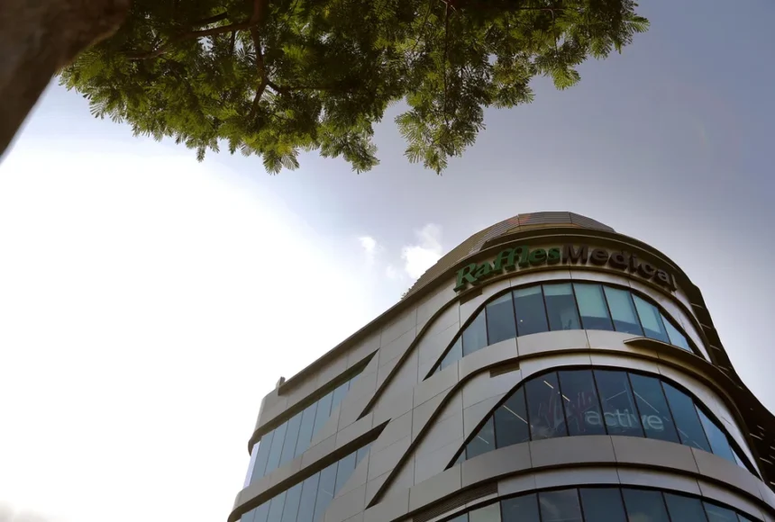 Low angle shot of the modern Raffles Medical building facade against a clear sky with green foliage.