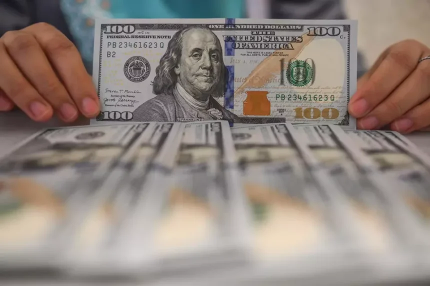 Hands holding a 100 dollar bill over stacks of cash, illustrating the exchange rate between the USD and the Rupiah.