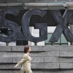 A pedestrian walks past the large SGX logo outside the building, representing the market for Singapore stocks.