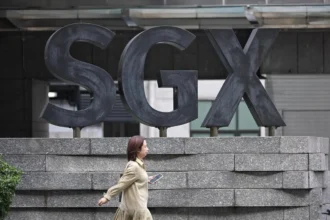 A pedestrian walks past the large SGX logo outside the building, representing the market for Singapore stocks.