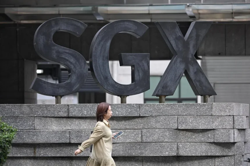 A pedestrian walks past the large SGX logo outside the building, representing the market for Singapore stocks.