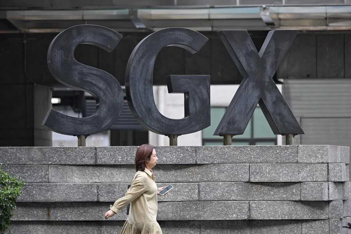 A pedestrian walks past the large SGX logo outside the building, representing the market for Singapore stocks.