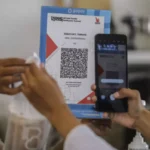 A customer scans a QRIS code to complete a cross border transaction via the Alipay network using a mobile app.