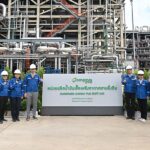 A group of officials in hard hats stands in front of the BCP sustainable aviation fuel industrial plant.