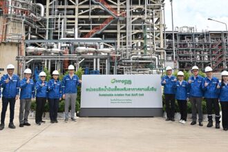 A group of officials in hard hats stands in front of the BCP sustainable aviation fuel industrial plant.