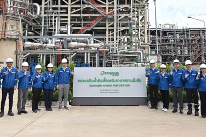 A group of officials in hard hats stands in front of the BCP sustainable aviation fuel industrial plant.