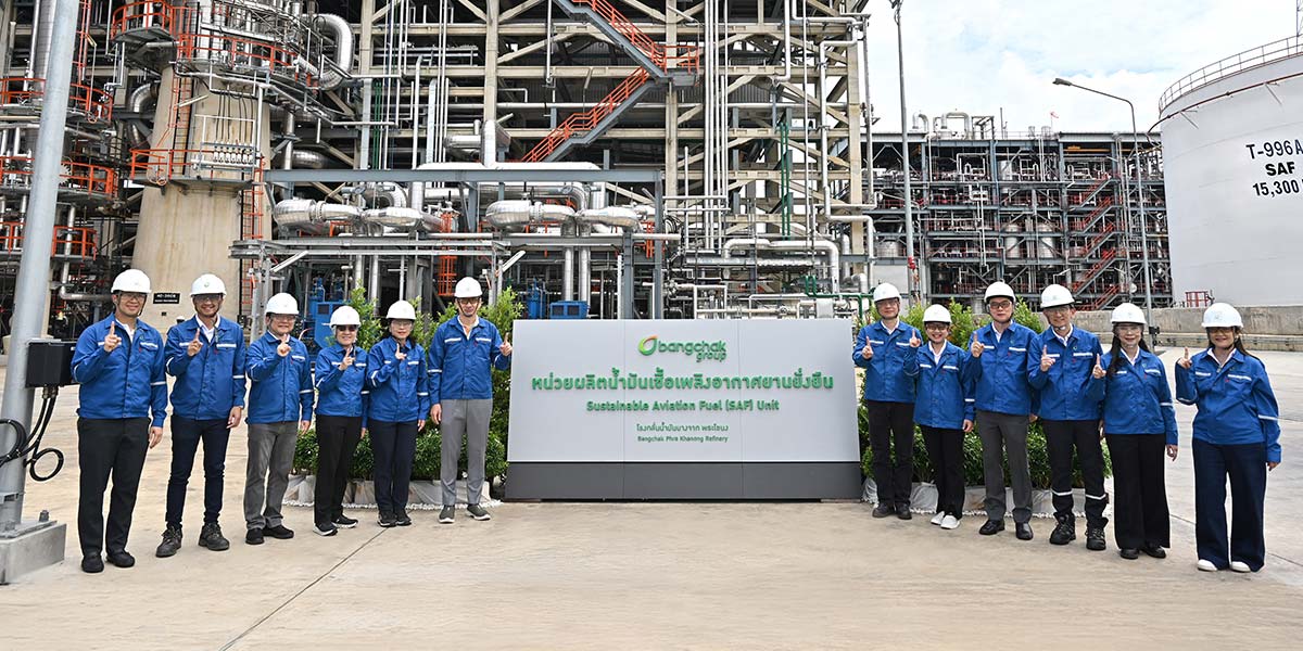 A group of officials in hard hats stands in front of the BCP sustainable aviation fuel industrial plant.