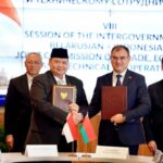 Indonesian and Belarusian officials shake hands while holding signed trade agreements at a joint commission meeting.
