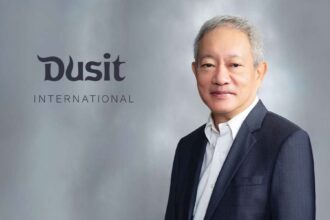 A professional studio portrait of Chanin Donavanik next to the grey Dusit International corporate logo.