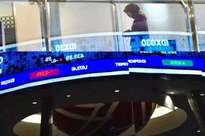 A person walking past a digital stock ticker displaying financial data and market trends related to the JCI at the IDX.
