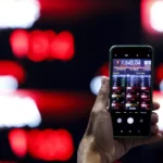 A mobile device displaying a downward trading session for the JCI against a blurry digital board.