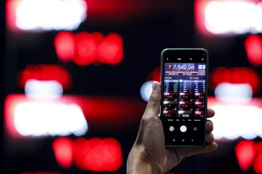 A mobile device displaying a downward trading session for the JCI against a blurry digital board.