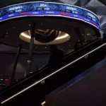 A woman on an escalator in front of a digital ticker showing the JCI and other market indices