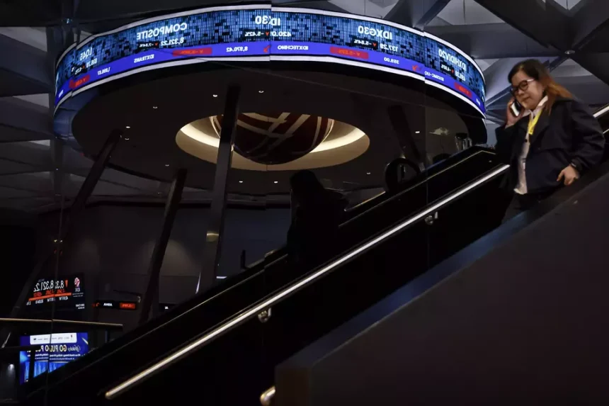 A woman on an escalator in front of a digital ticker showing the JCI and other market indices