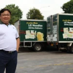 Lim Tze Chiang standing proudly in front of Leong Guan delivery trucks carrying fresh noodle products.