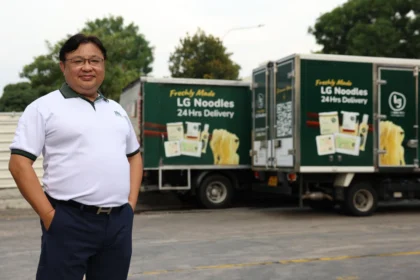 Lim Tze Chiang standing proudly in front of Leong Guan delivery trucks carrying fresh noodle products.