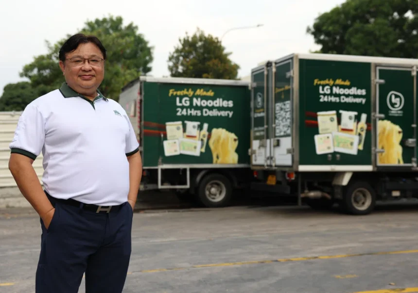 Lim Tze Chiang standing proudly in front of Leong Guan delivery trucks carrying fresh noodle products.