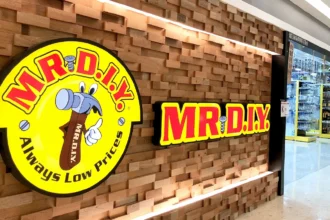 A storefront featuring the yellow and red Mr. DIY logo on a textured wood wall with bright store lighting.