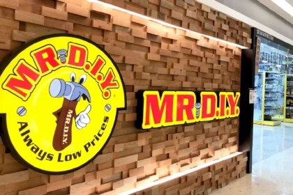 A storefront featuring the yellow and red Mr. DIY logo on a textured wood wall with bright store lighting.