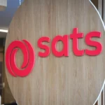 The company logo for SATS displayed on a wooden circular sign