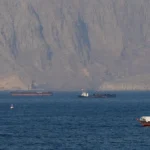 Vessels navigating critical oil shipping lanes near the Strait of Hormuz against a rugged mountainous coastline.