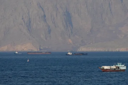 Vessels navigating critical oil shipping lanes near the Strait of Hormuz against a rugged mountainous coastline.