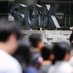 A large outdoor sign for the SGX Group stands behind a crowd of commuters, symbolizing the home market for suspended firms.