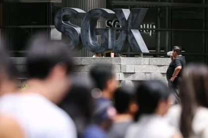 A large outdoor sign for the SGX Group stands behind a crowd of commuters, symbolizing the home market for suspended firms.