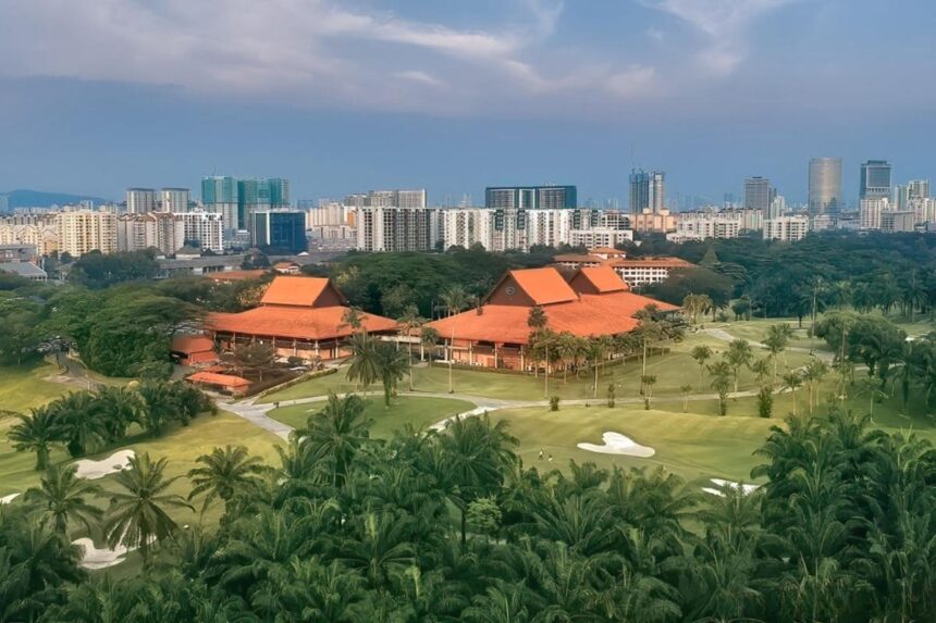 Aerial view of the lush greenery and clubhouse at Saujana Resort set against a modern city skyline.