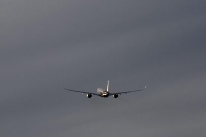Commercial airplane flying through a cloudy sky, representing global summer travel.
